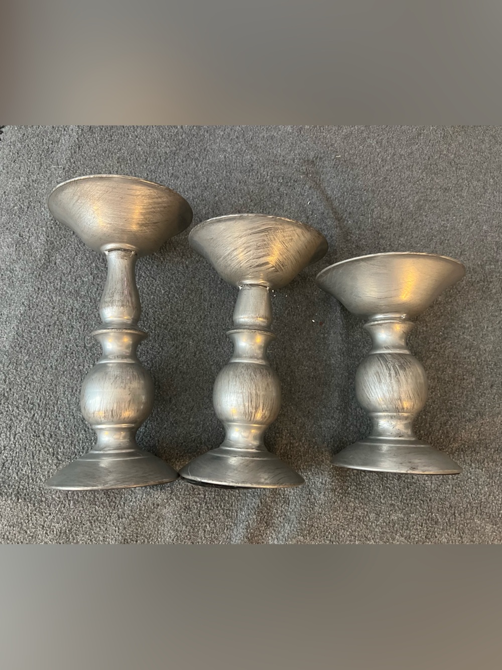 set of three silver-tone metal candlestick holders features a graduated design